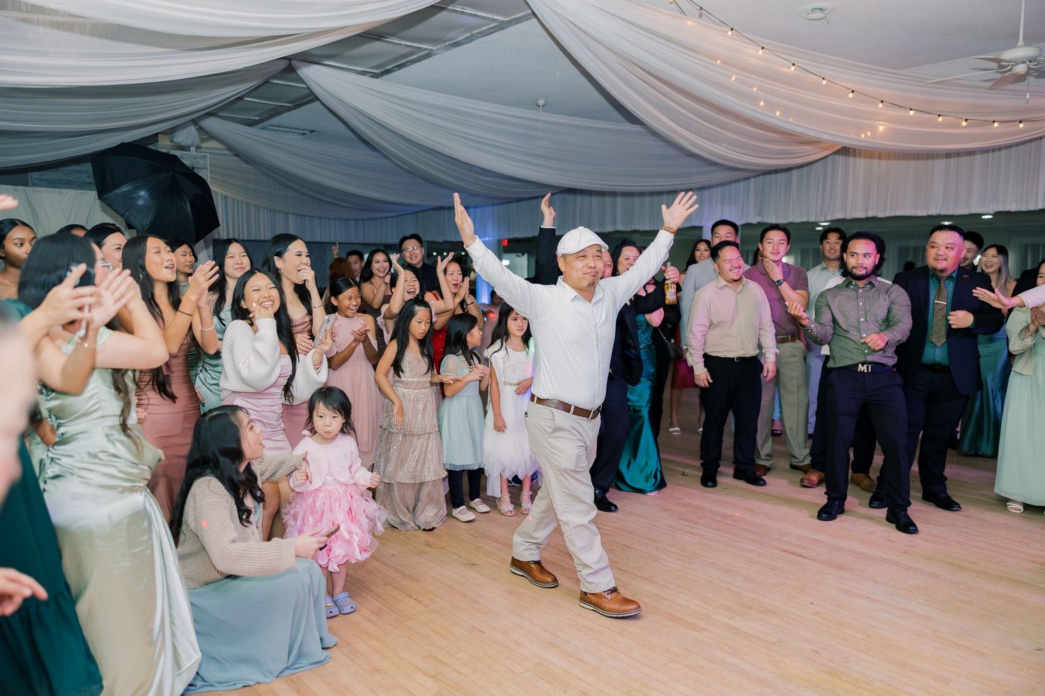 Wedding guests dancing and celebrating on a dance floor under white tent decorations at an outdoor reception.
