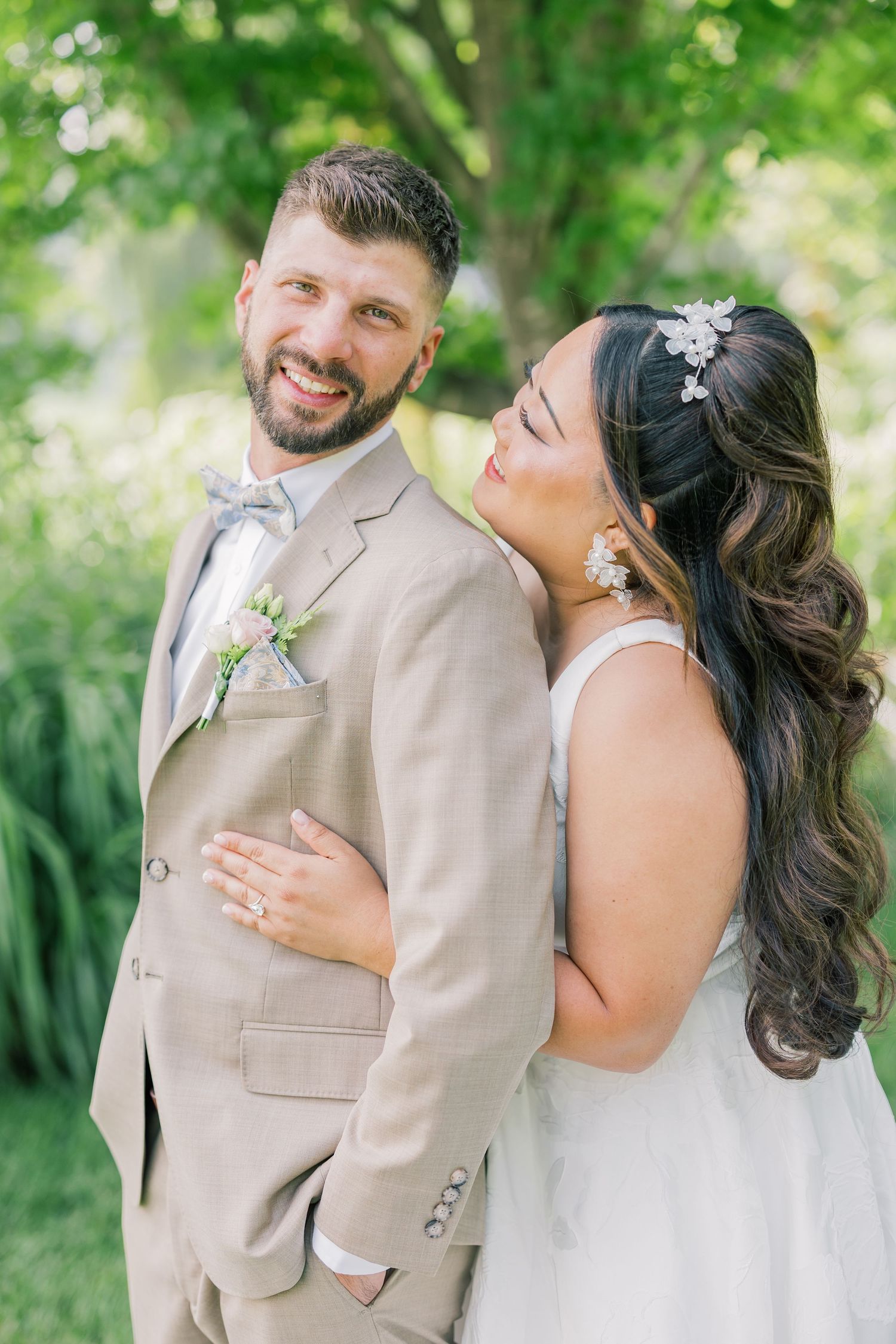 A couple shares an intimate moment in their wedding attire against a lush green outdoor backdrop.