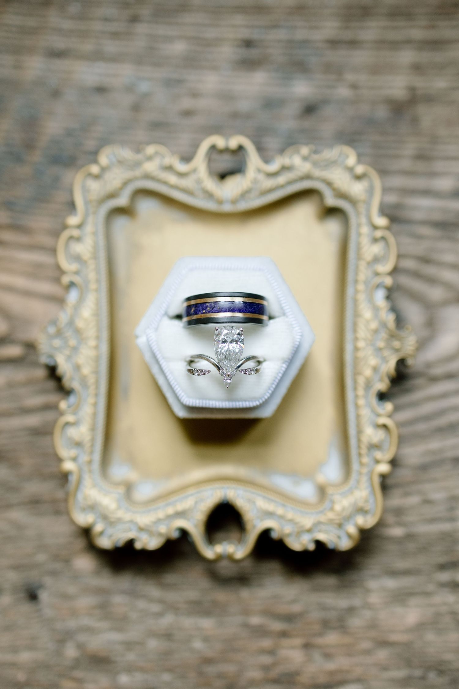 Wedding rings displayed on ornate cream-colored frames against rustic wooden background.