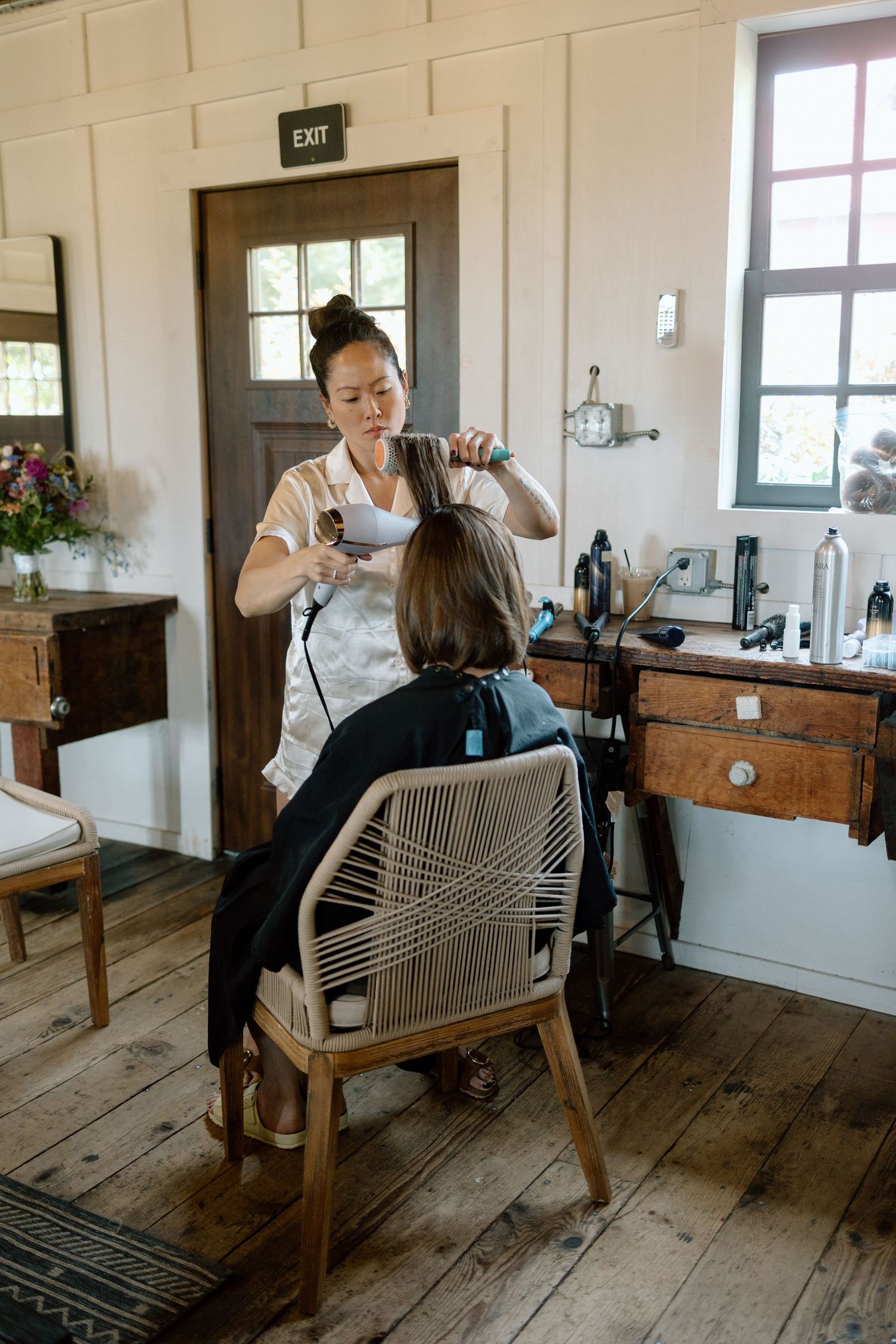 A stylist works on a client's hair in a rustic salon with wooden floors and vintage furniture.