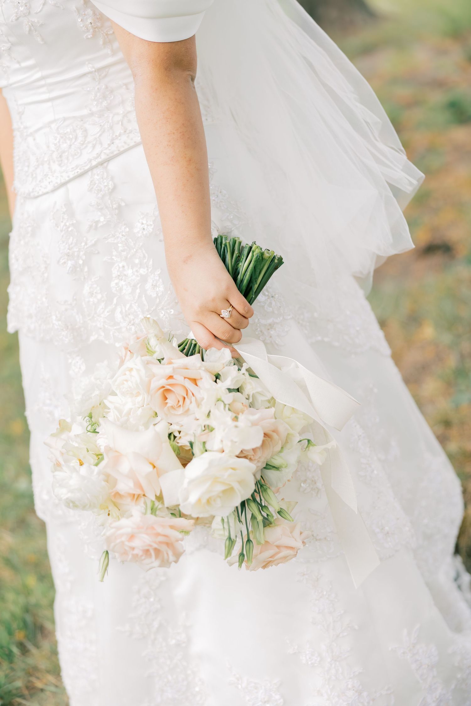 A delicate blush and white bridal bouquet with cascading flowers held against a flowing white wedding dress.