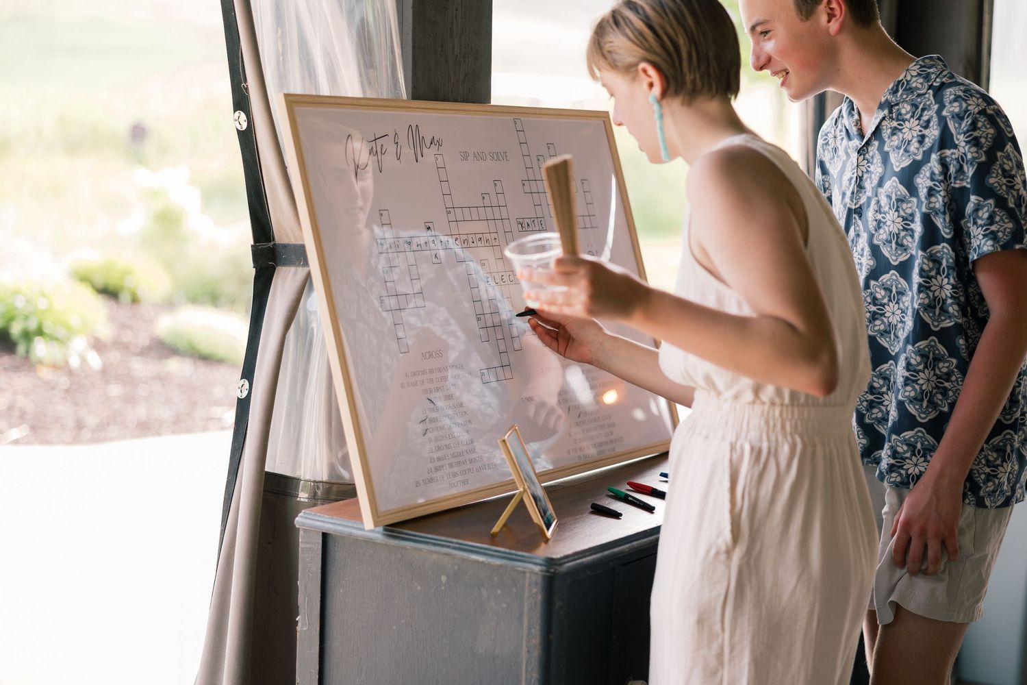 Wedding guests sign messages on white easel boards at an indoor reception.