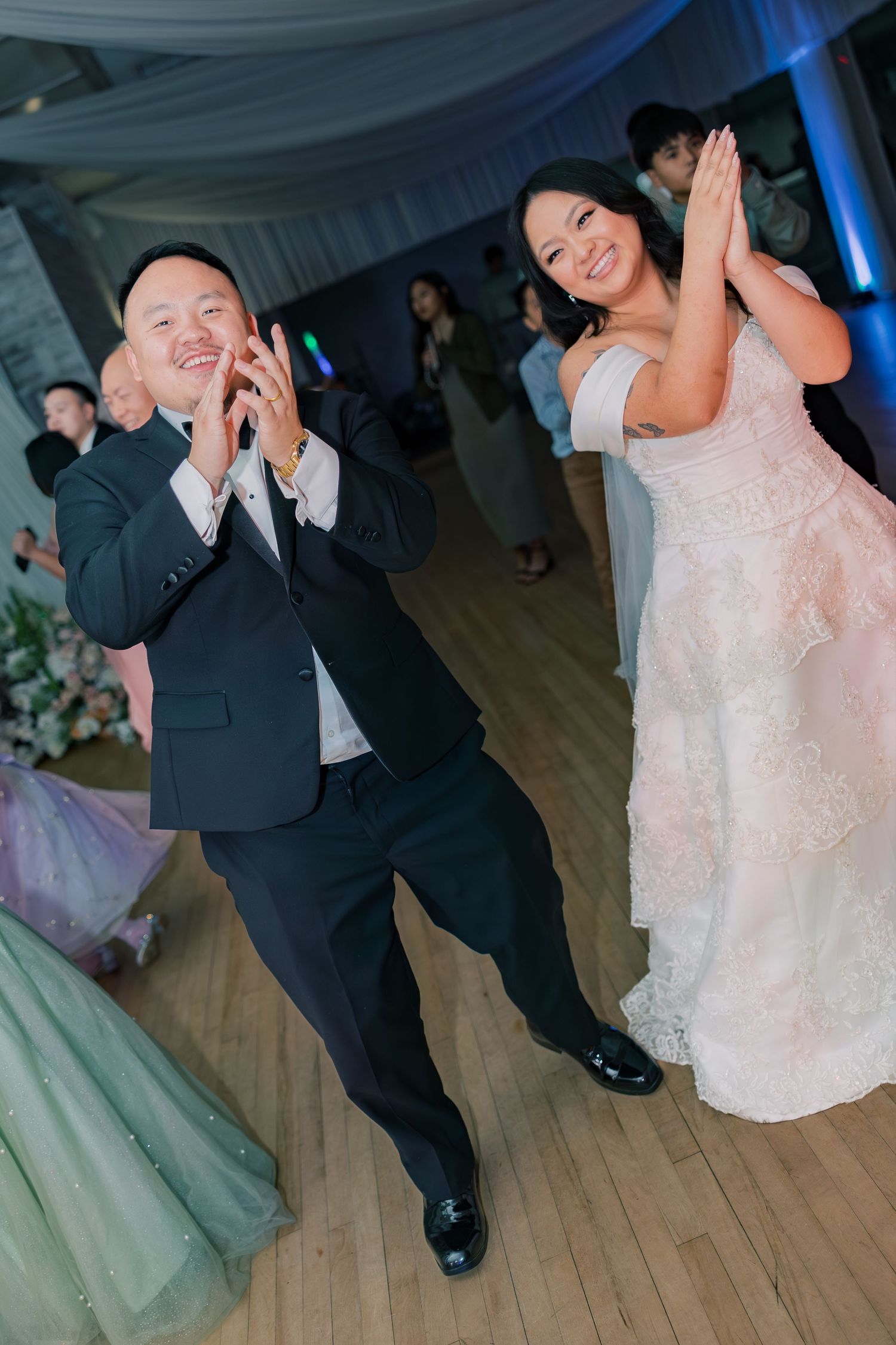 Dynamic dance sequence at a wedding reception with blue lighting and wooden floors.