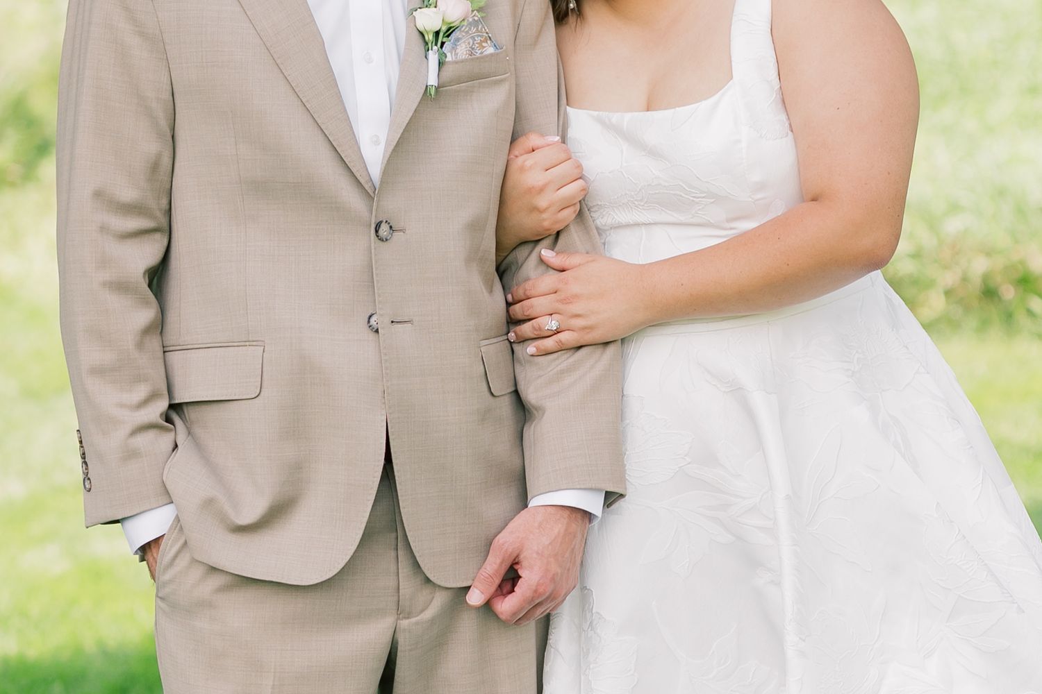 Elegant wedding couple in white dress and tan suit posing in garden setting.