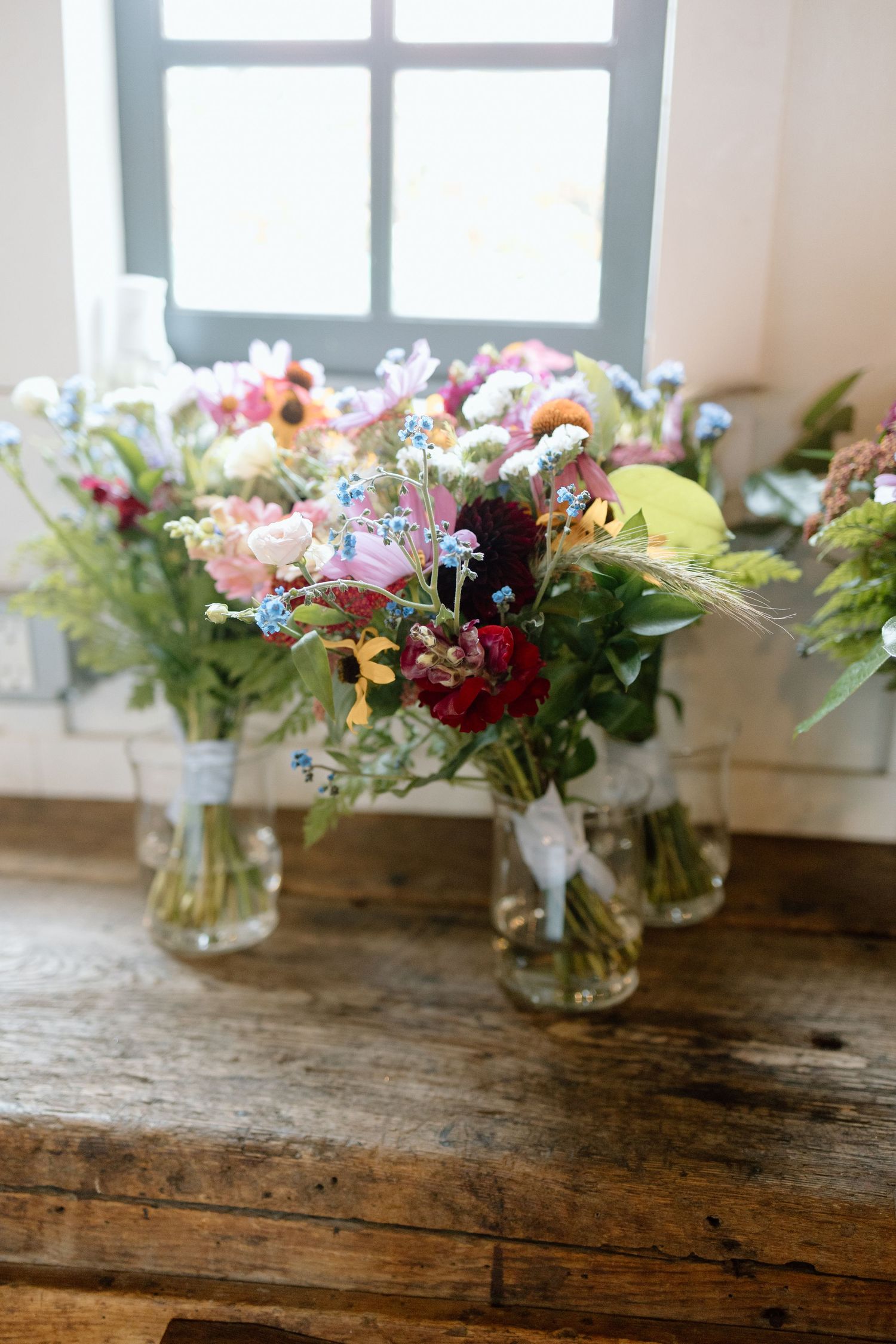 Colorful wildflower bouquets in mason jars displayed on a rustic wooden table near a window.