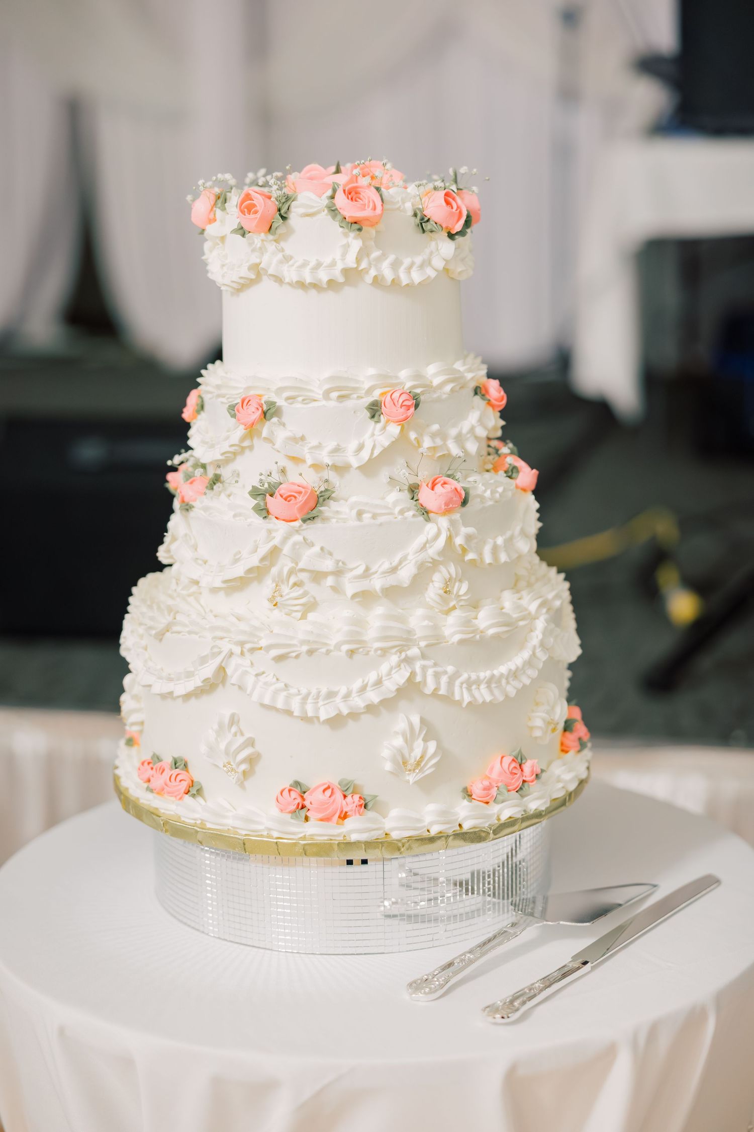 Elegant three-tier white wedding cake decorated with delicate piping and small coral-colored roses on display.
