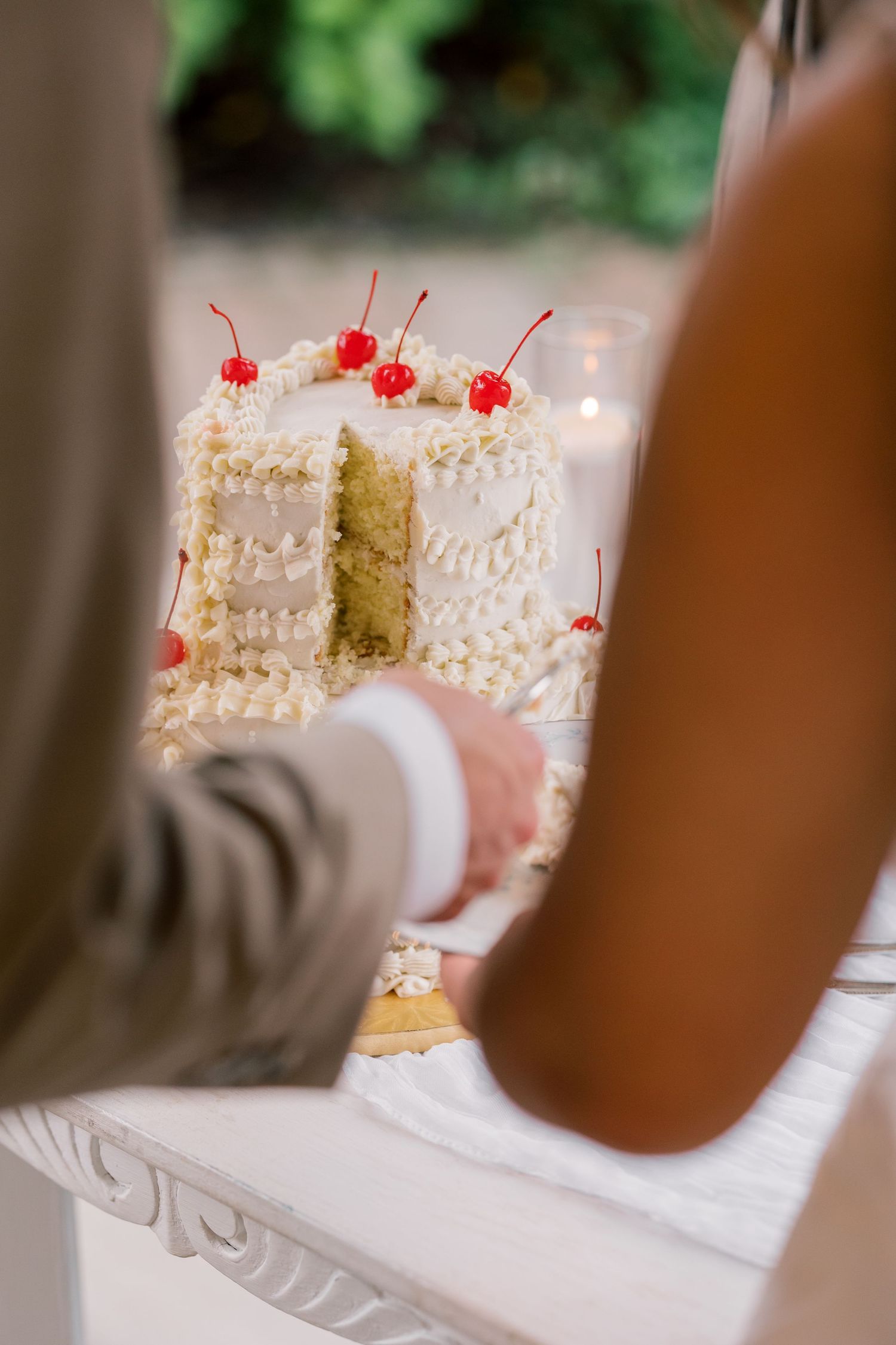 Close-up shots of an elegant white wedding cake decorated with cherries and pearl details.