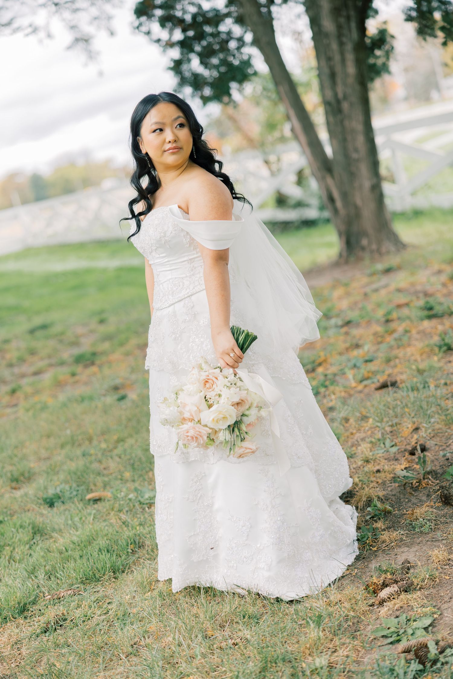 An elegant bridal portrait outdoors with lace dress and soft pink bouquet.