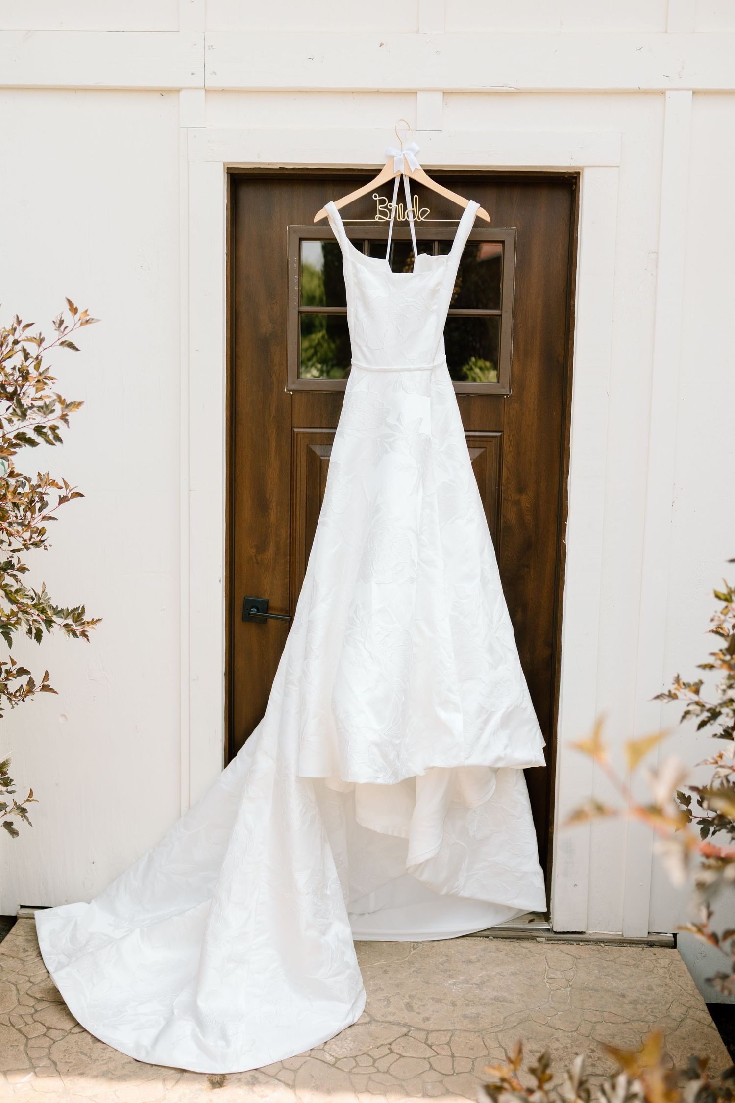 An elegant white wedding dress with a long train hangs displayed against a wooden door.