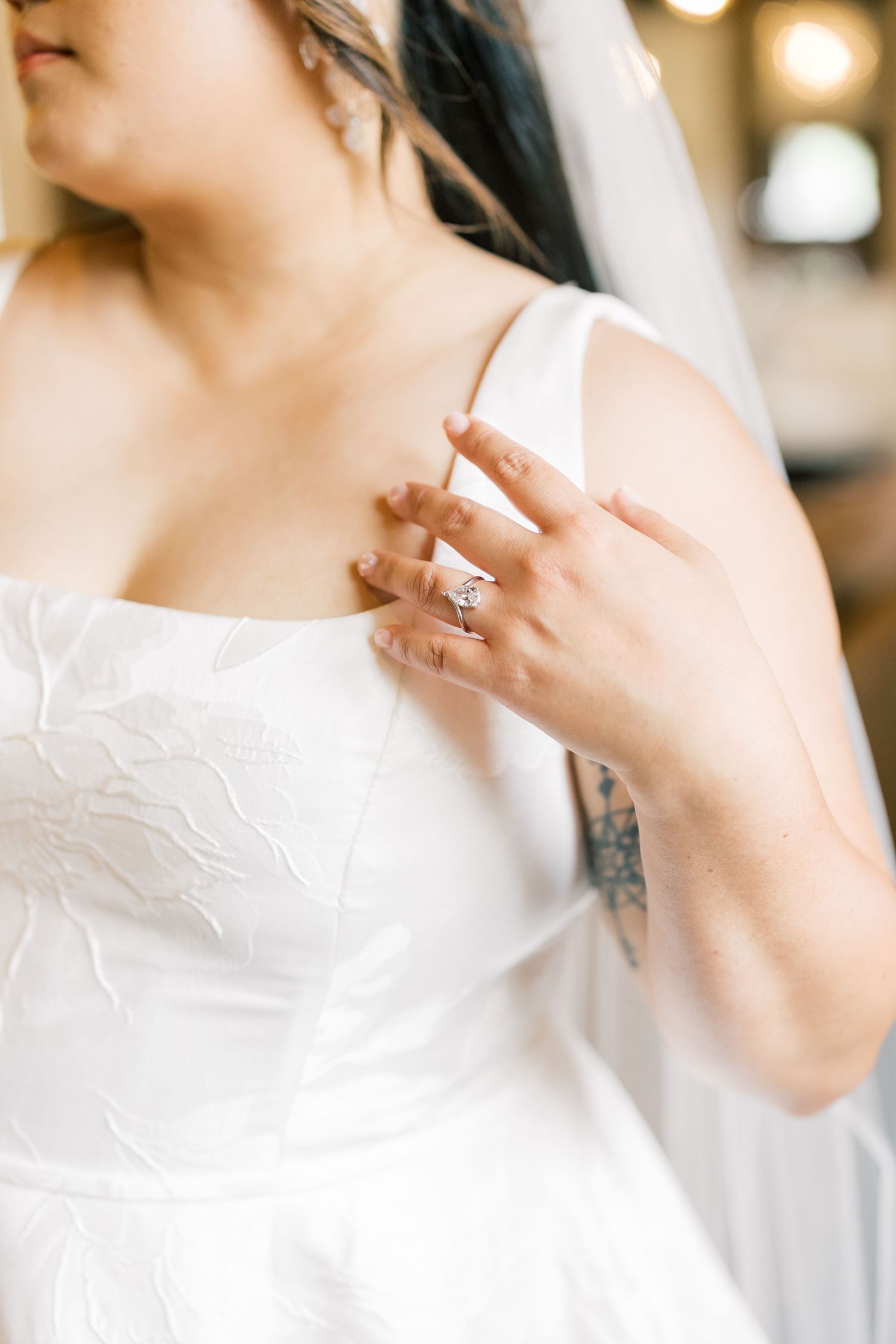 Close-up view of a white lace wedding dress detail with an engagement ring.