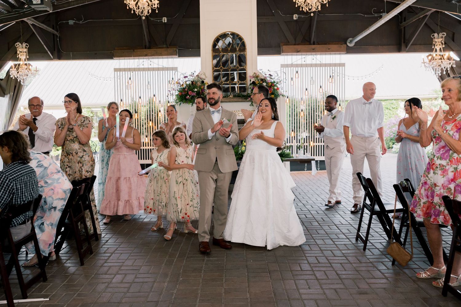 Wedding reception in a rustic venue with chandeliers and guests lining the aisle.
