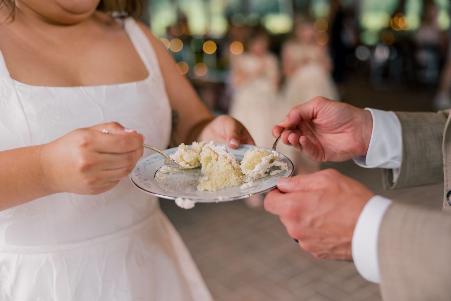 Close-up of hands serving wedding cake on white plates at reception.