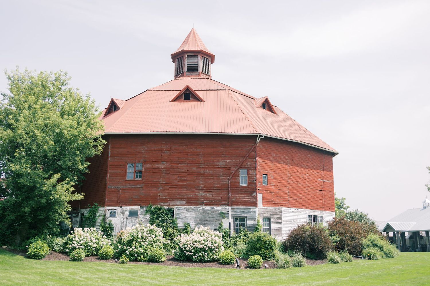 Panoramic view of a large red round barn with white trim and cupola set against a cloudy sky.