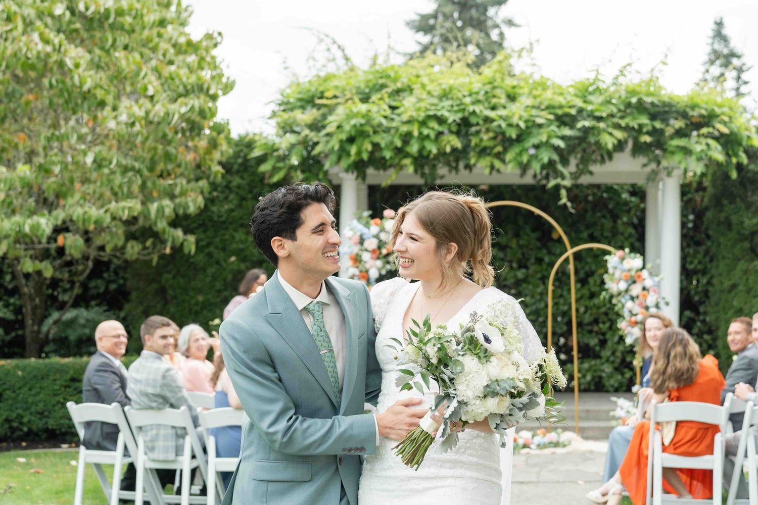 Wedding celebration outdoors with couples dancing and embracing under white tent during daytime reception.