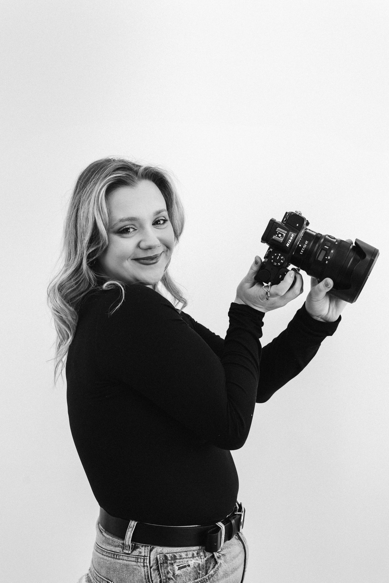 Black and white portrait of a smiling blonde female photographer holding a professional camera.