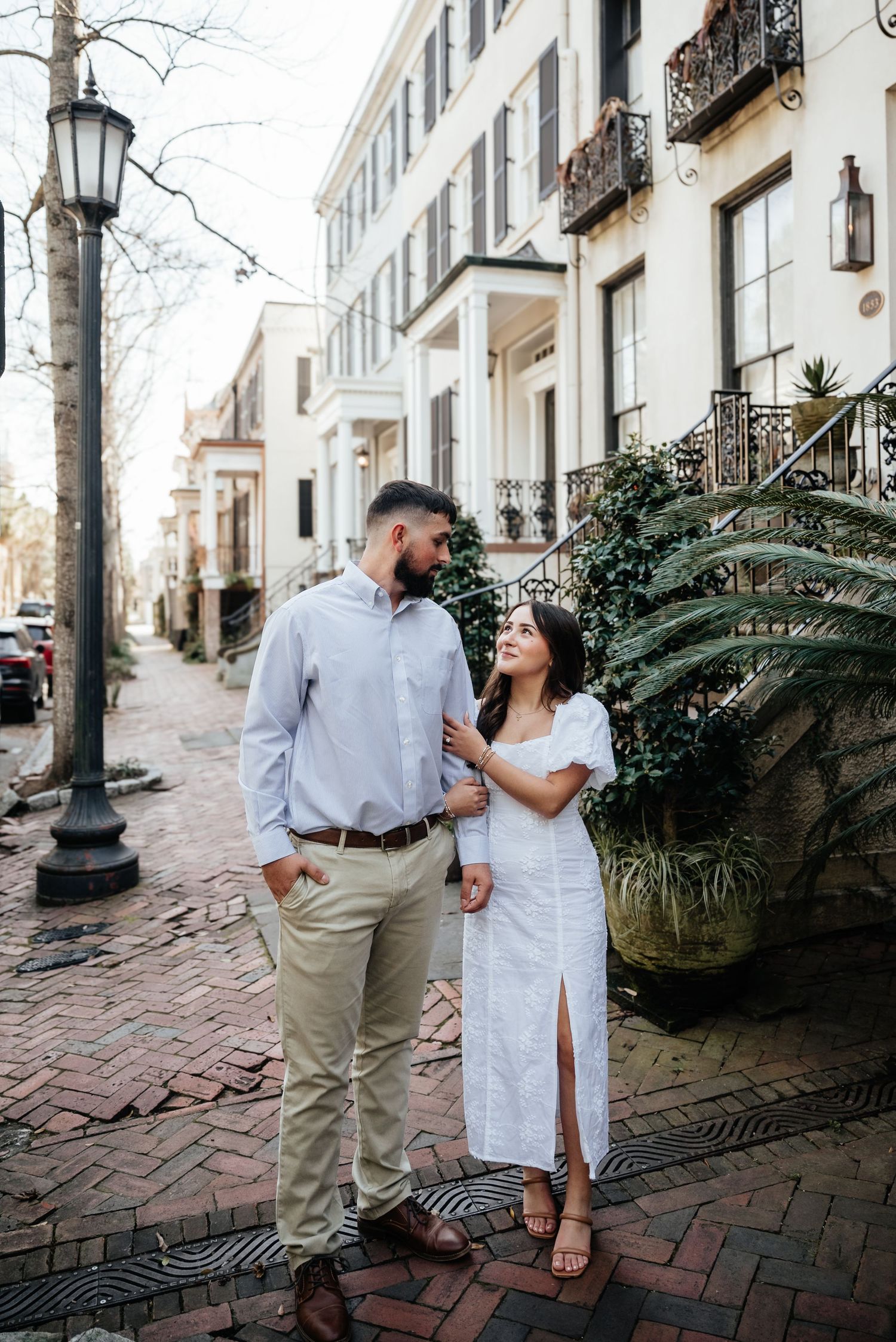 Couple in love walking on a brick sidewalk lined with historic Southern architecture.