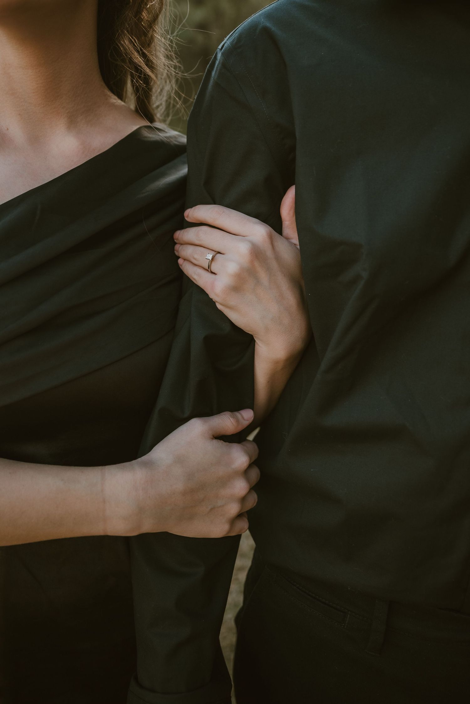 Close-up of a couple in black formal wear, woman's hand with engagement ring gently holding man's suit jacket.