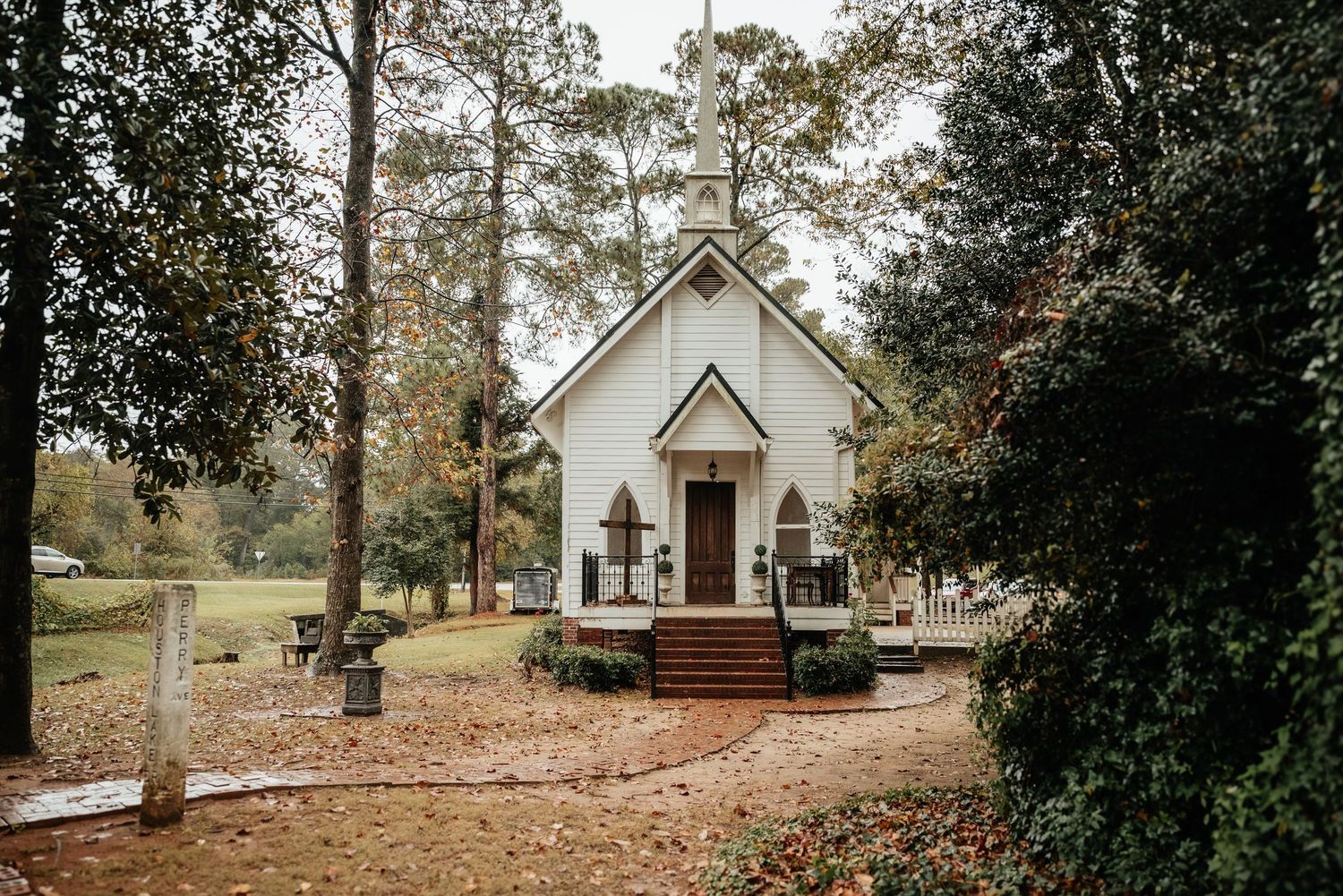 A charming white country church surrounded by autumn trees and fallen leaves in a serene rural setting.