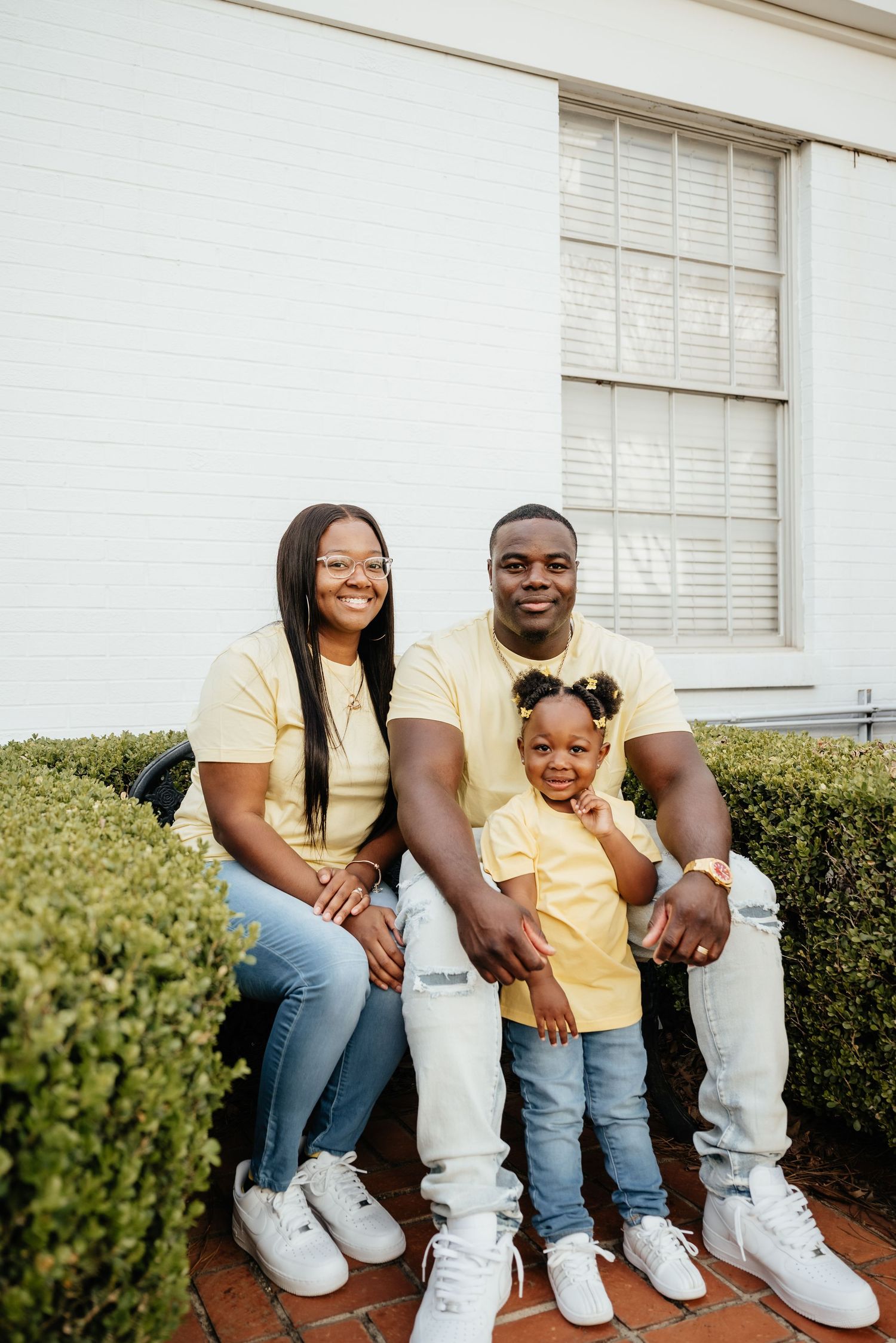 A happy family of three wearing matching yellow outfits poses together on brick steps outside.