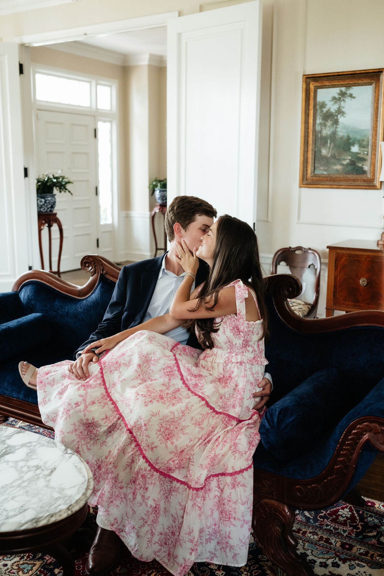 Couple shares a kiss while seated on a vintage blue velvet sofa during an indoor engagement session.