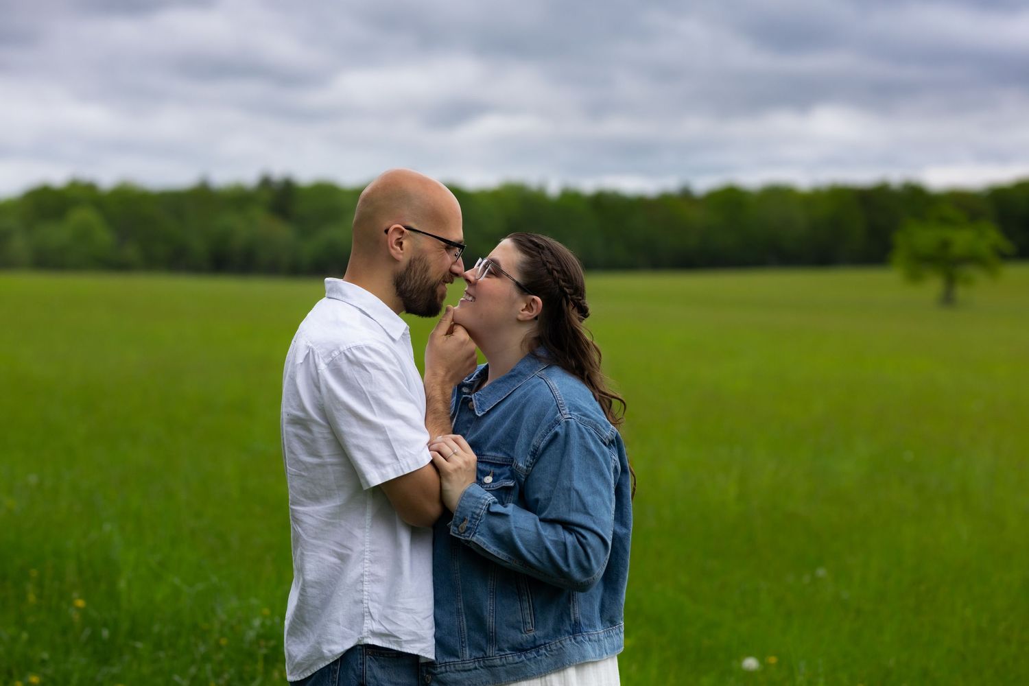 A couple shares an intimate moment while standing in a lush green meadow under cloudy skies.