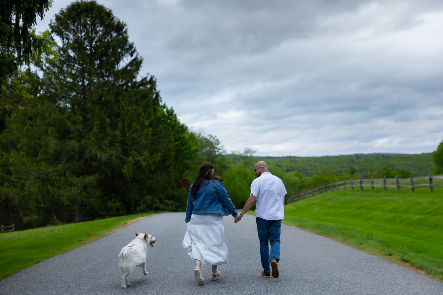 People walking along a scenic trail on a cloudy day with lush green grass and trees in the background.