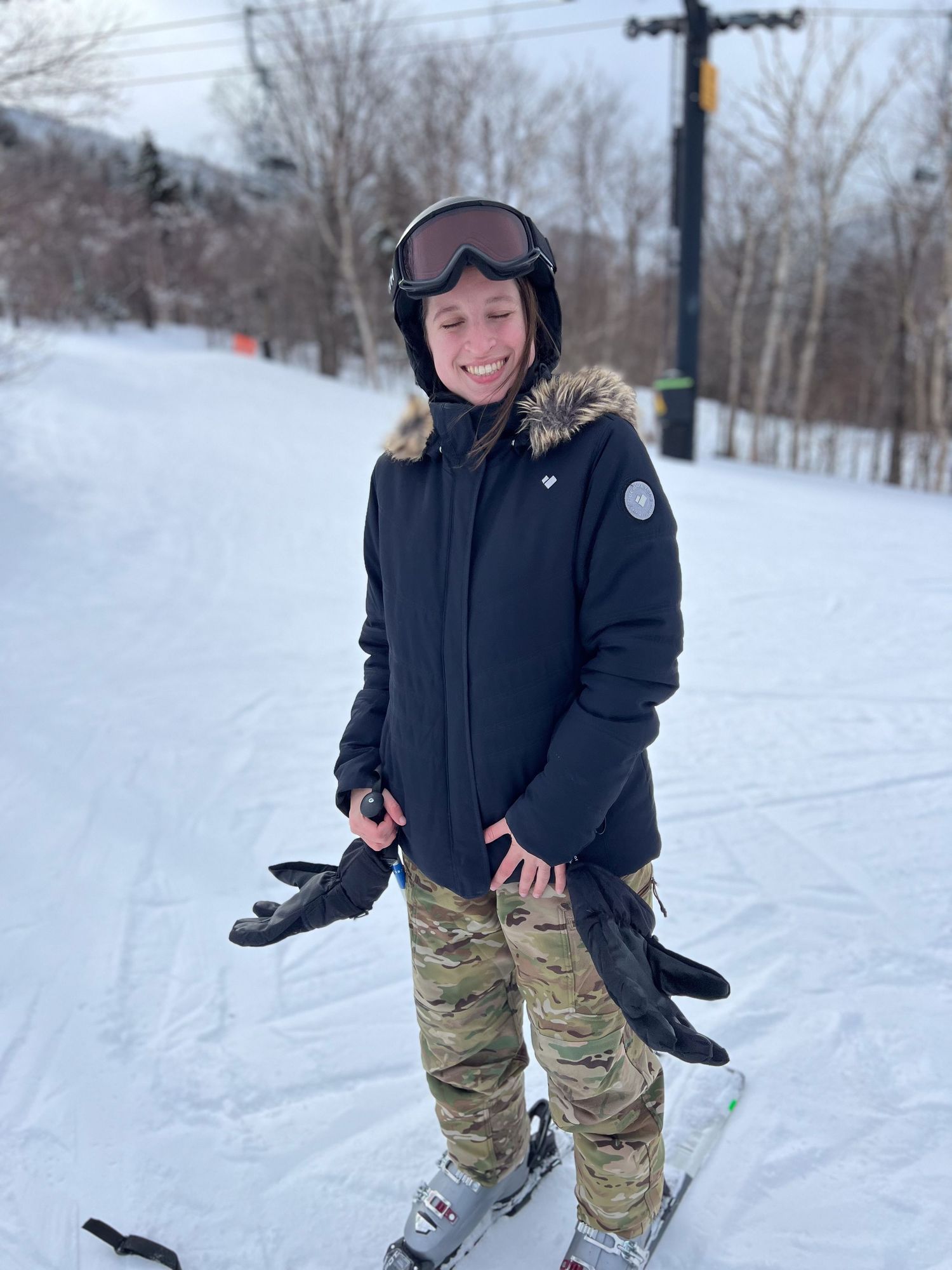 A skier in a black winter coat and camouflage pants practices turns on a snowy slope during a winter day.