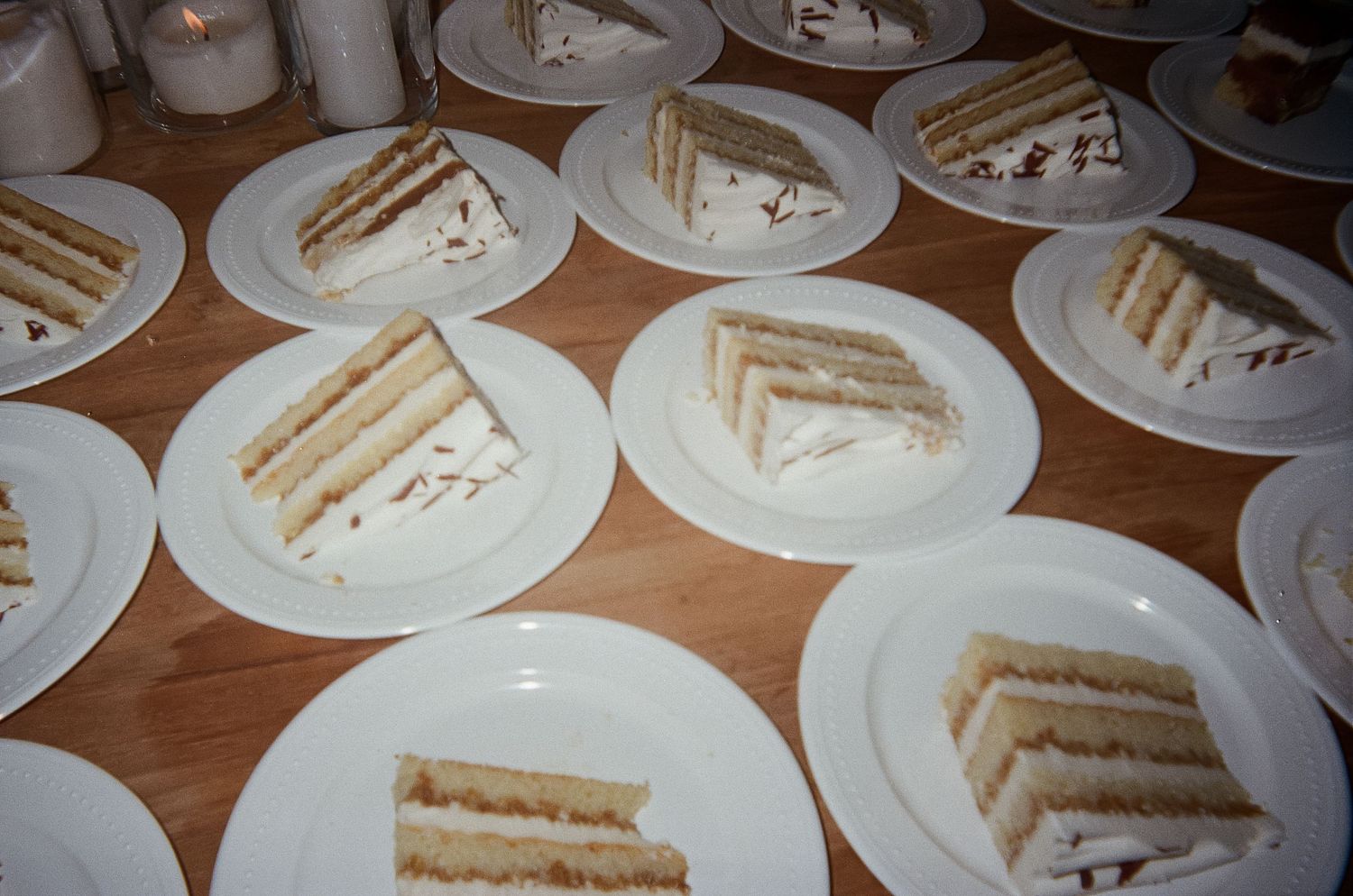 Multiple slices of layered cake on white plates arranged on a wooden surface. Film Photograph.