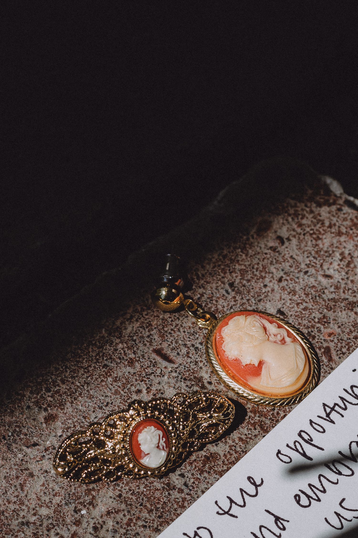 Vintage cameo jewelry and handwritten note on textured surface.
