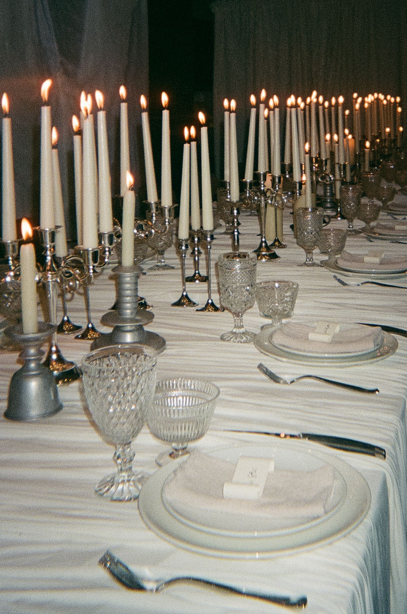 Elegant table setting with multiple crystal candlesticks and white tapered candles. Film Photograph.