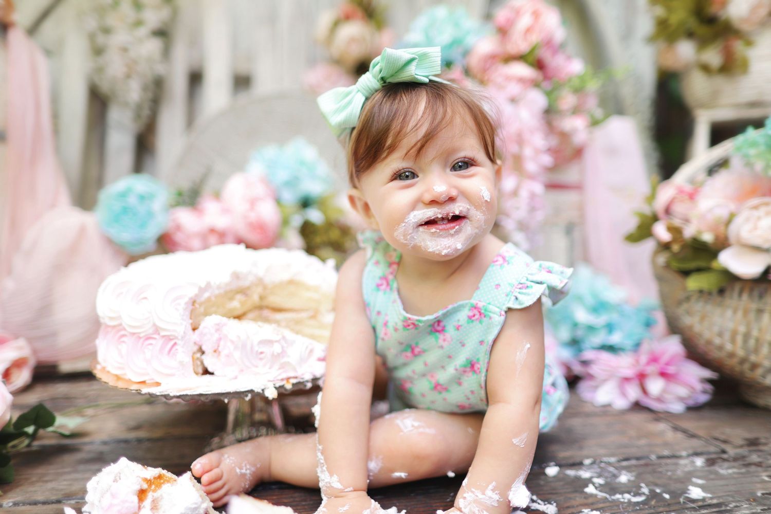 Happy baby girl sitting on floor smiling after cake smash with frosting on face.