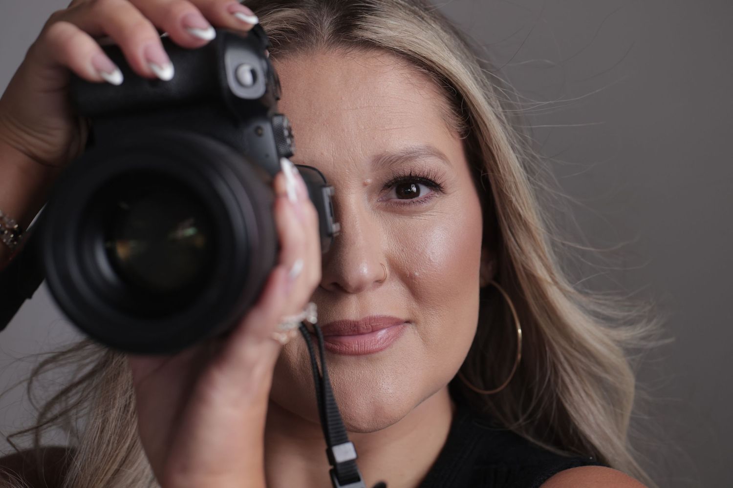 Blonde woman holding a professional DSLR camera up to her face in a studio setting.