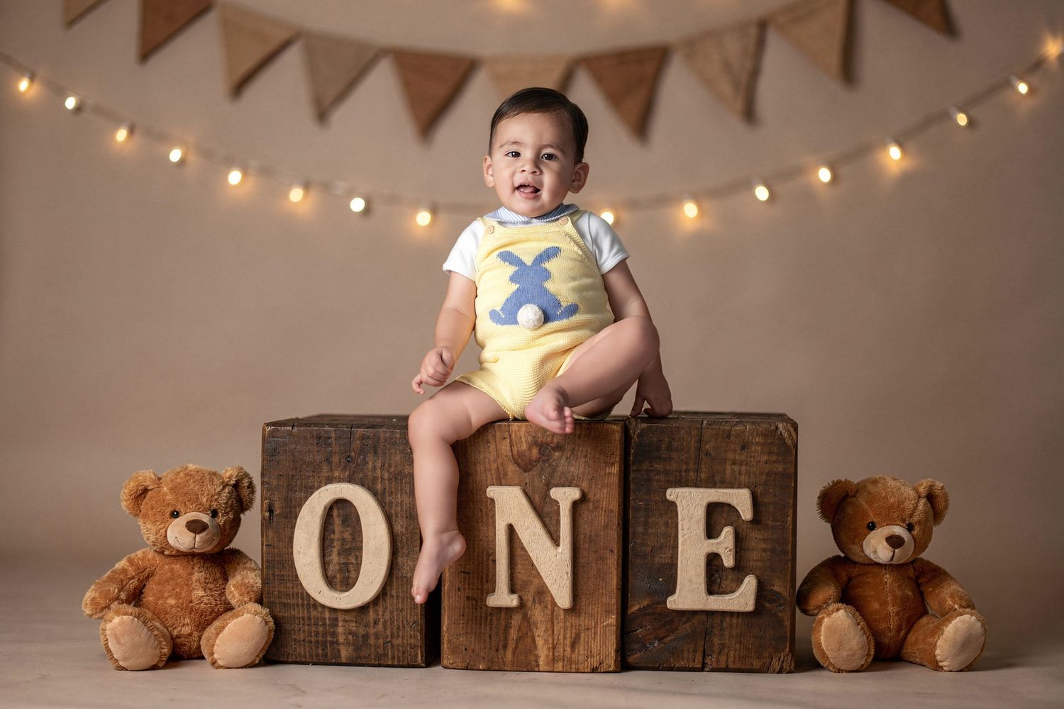 Baby boy sits on wooden ONE blocks with teddy bears for his first birthday photo session with string lights backdrop.