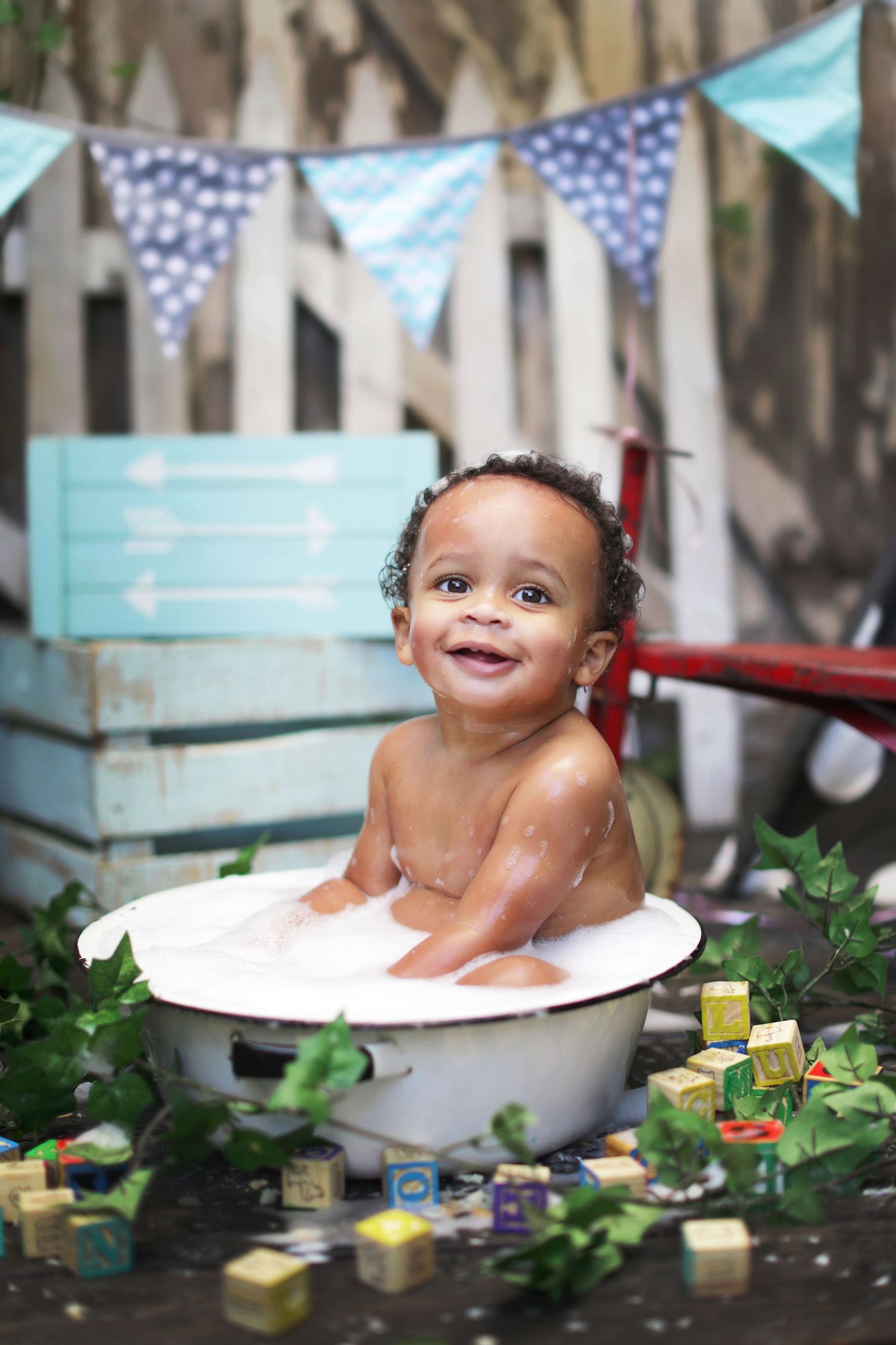 Happy African American baby boy splashes in vintage tub at outdoor first birthday celebration.