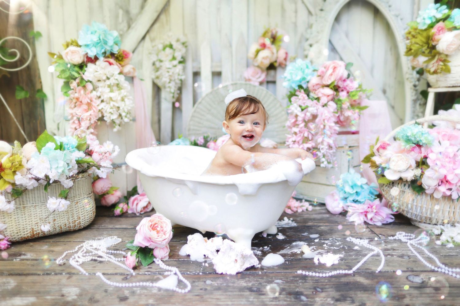 Smiling baby girl sitting in white clawfoot bathtub surrounded by colorful flowers.
