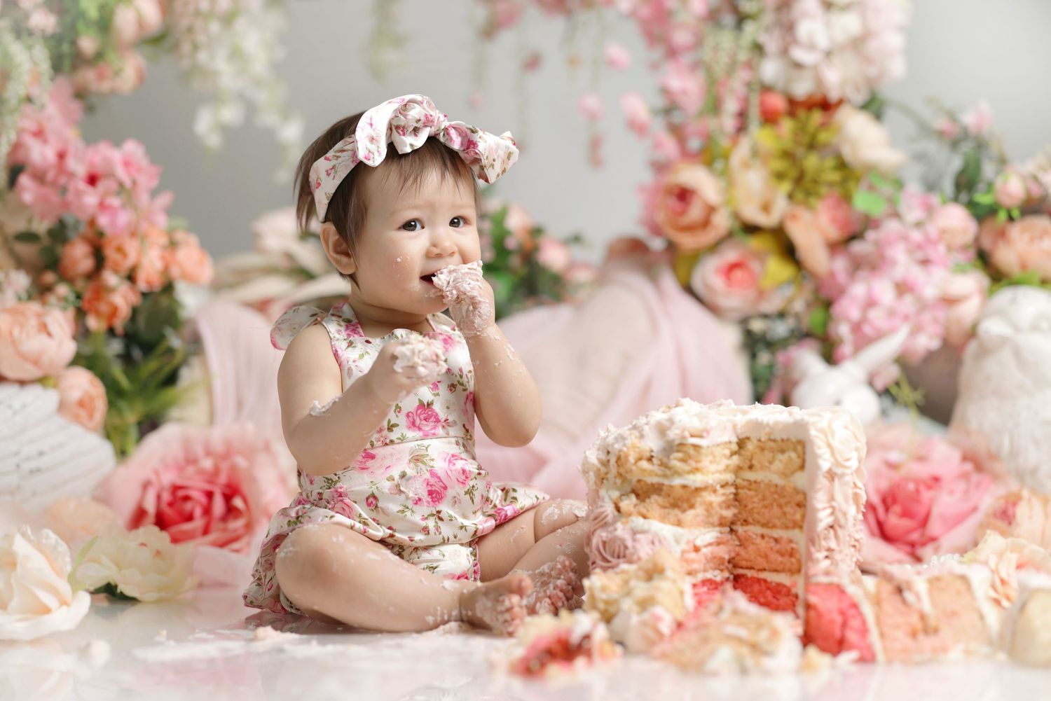 Baby girl in floral romper eating cake during pink rose garden cake smash photo session.