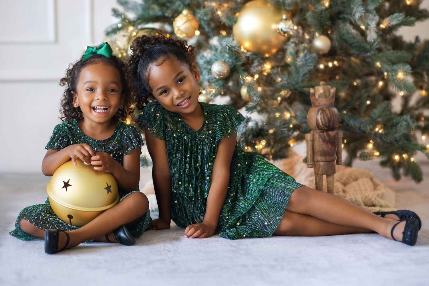 Two young girls in matching green dresses pose by a decorated Christmas tree with gold ornaments.