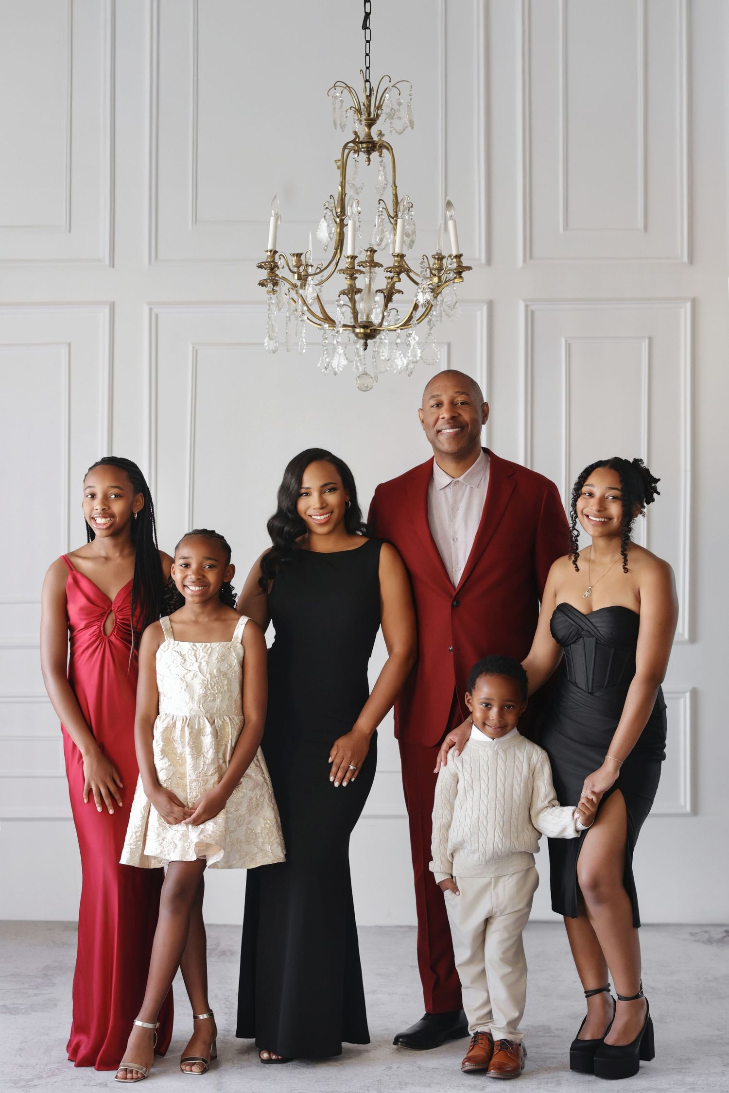 Elegant family portrait with six members dressed in formal attire, posing under a crystal chandelier.