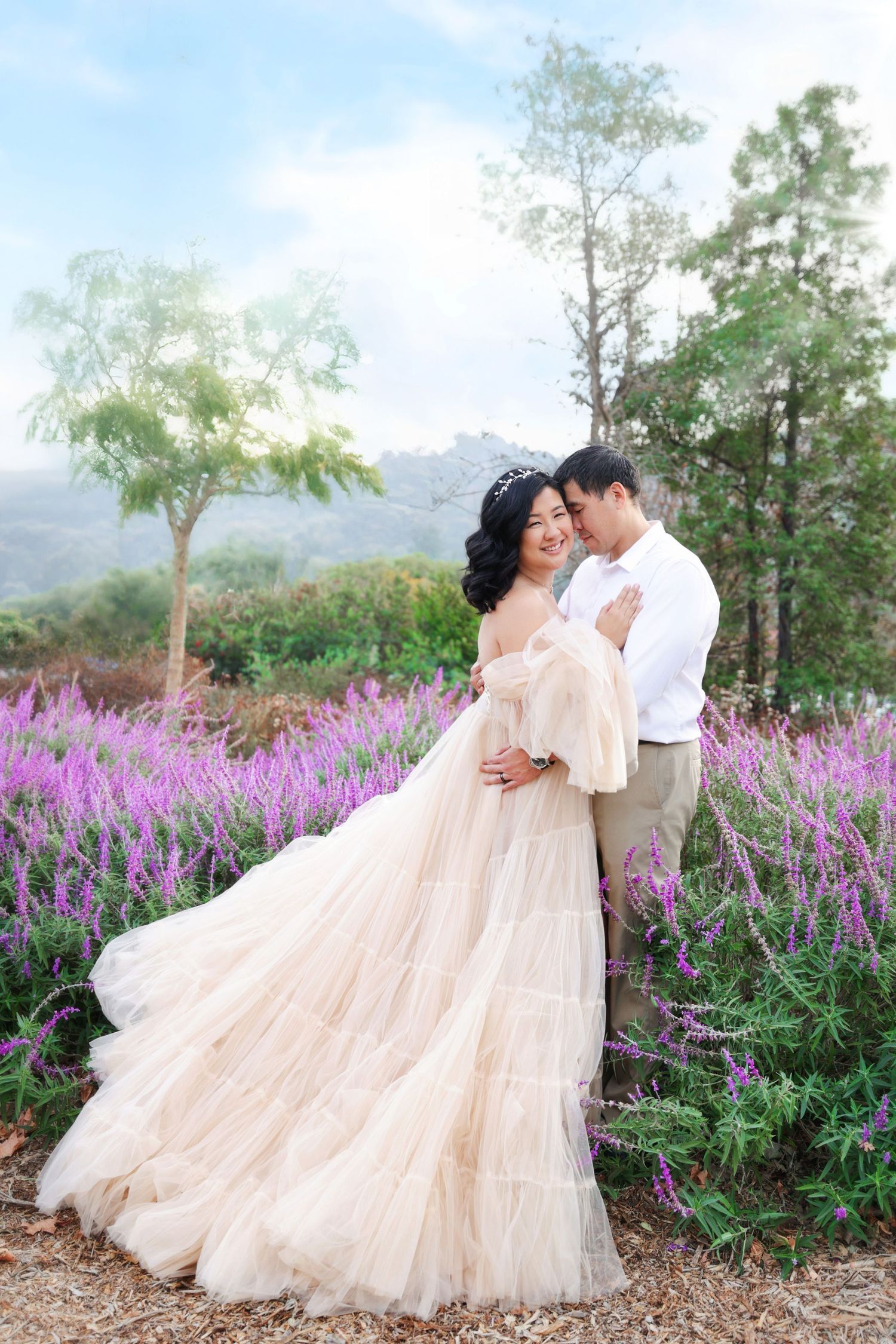 Couple in wedding attire embracing in a lavender field, bride wearing elegant champagne gown with flowing skirt.