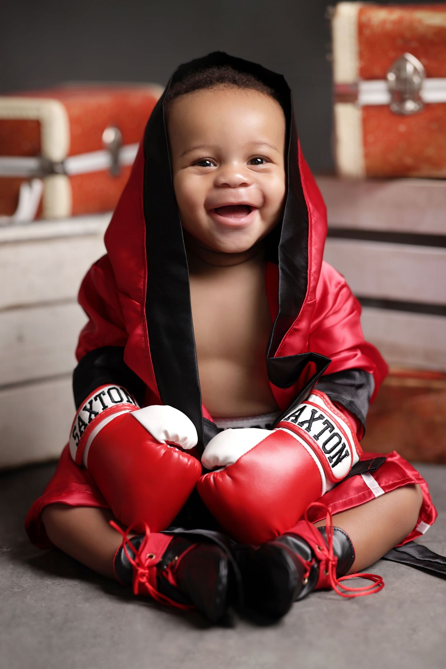Happy baby boy in red boxing robe and gloves smiling at camera.