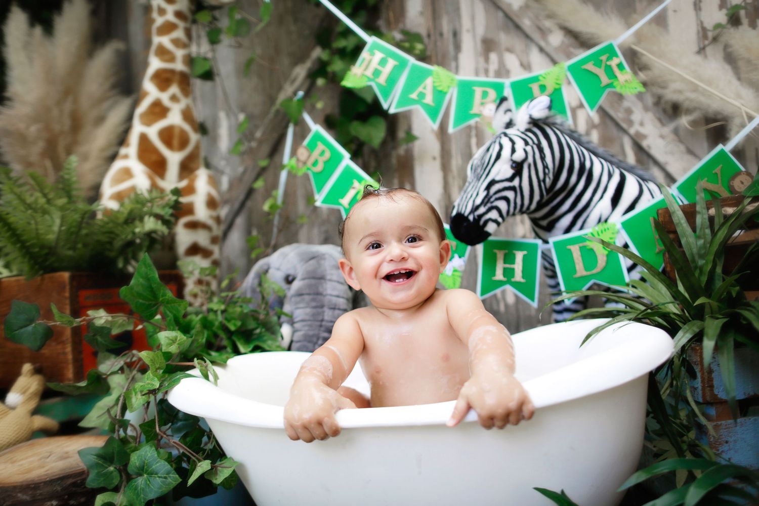Happy baby laughing in white bathtub at jungle safari themed first birthday photo session.