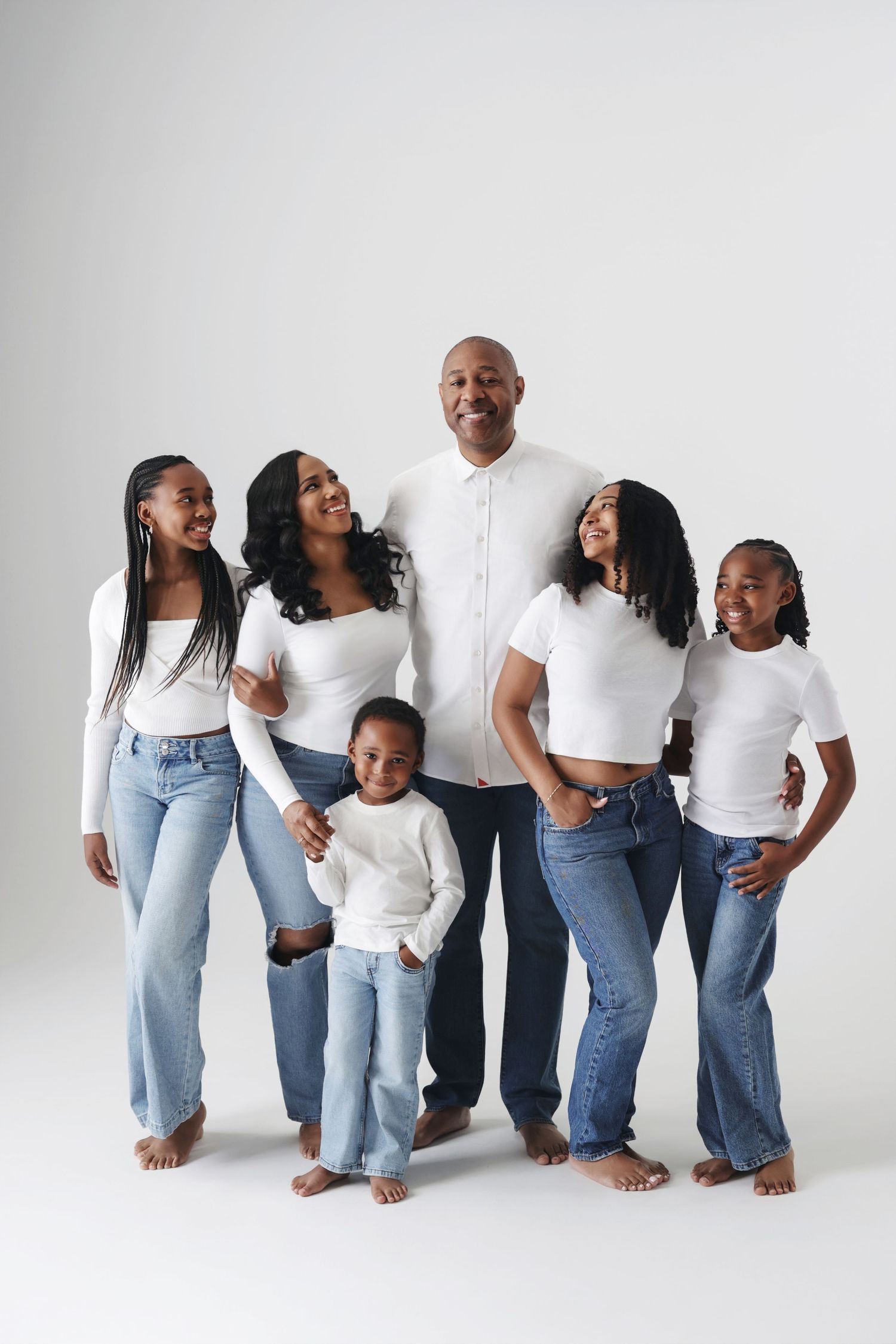 African American family of six posing in matching white tops and jeans against a white studio background.