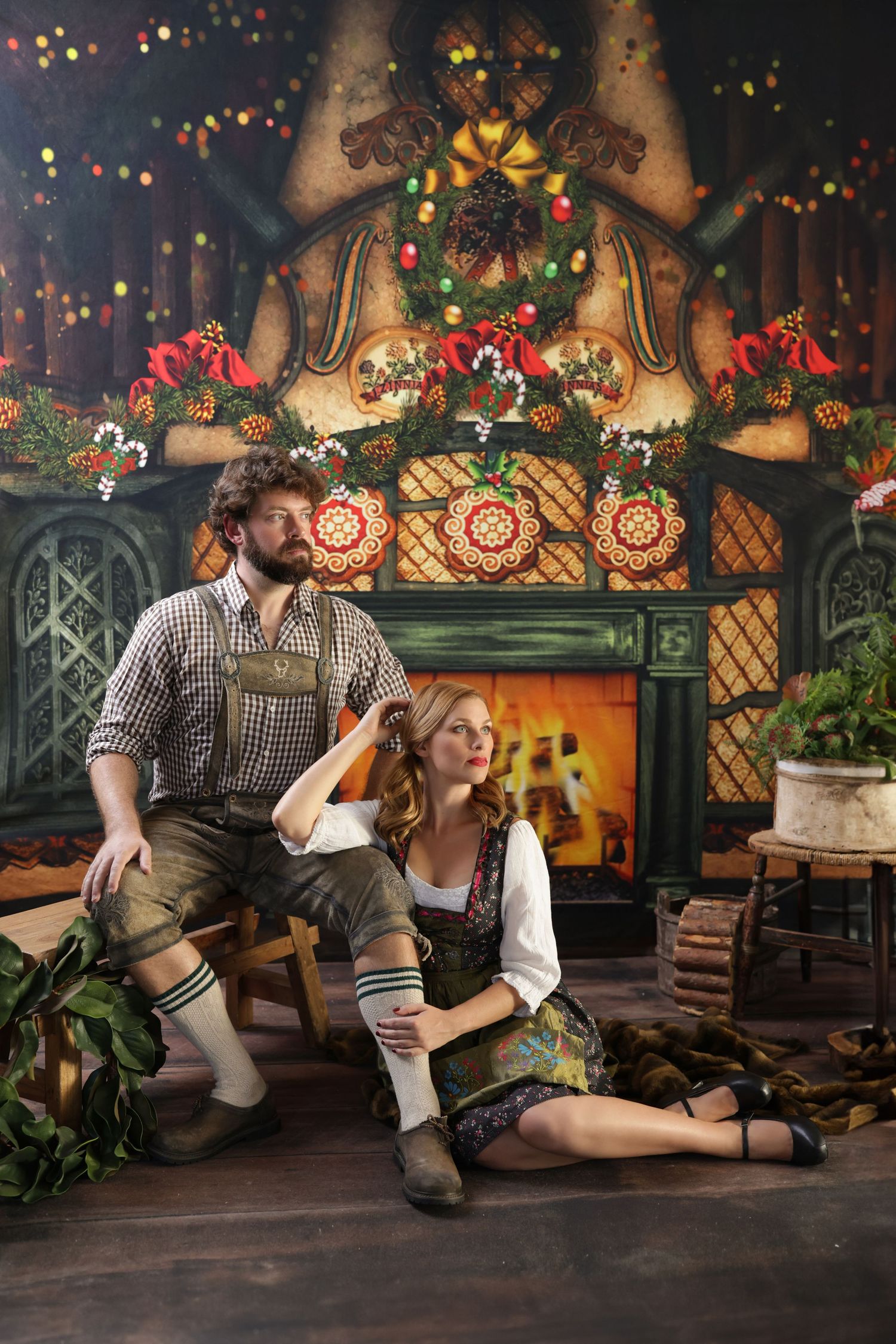 Couple in traditional Bavarian dirndl and lederhosen sitting by a decorated Christmas fireplace backdrop.