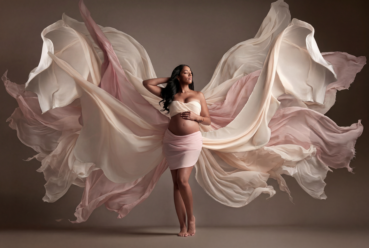 Elegant maternity photo of pregnant woman with flowing pink and white fabric wings.