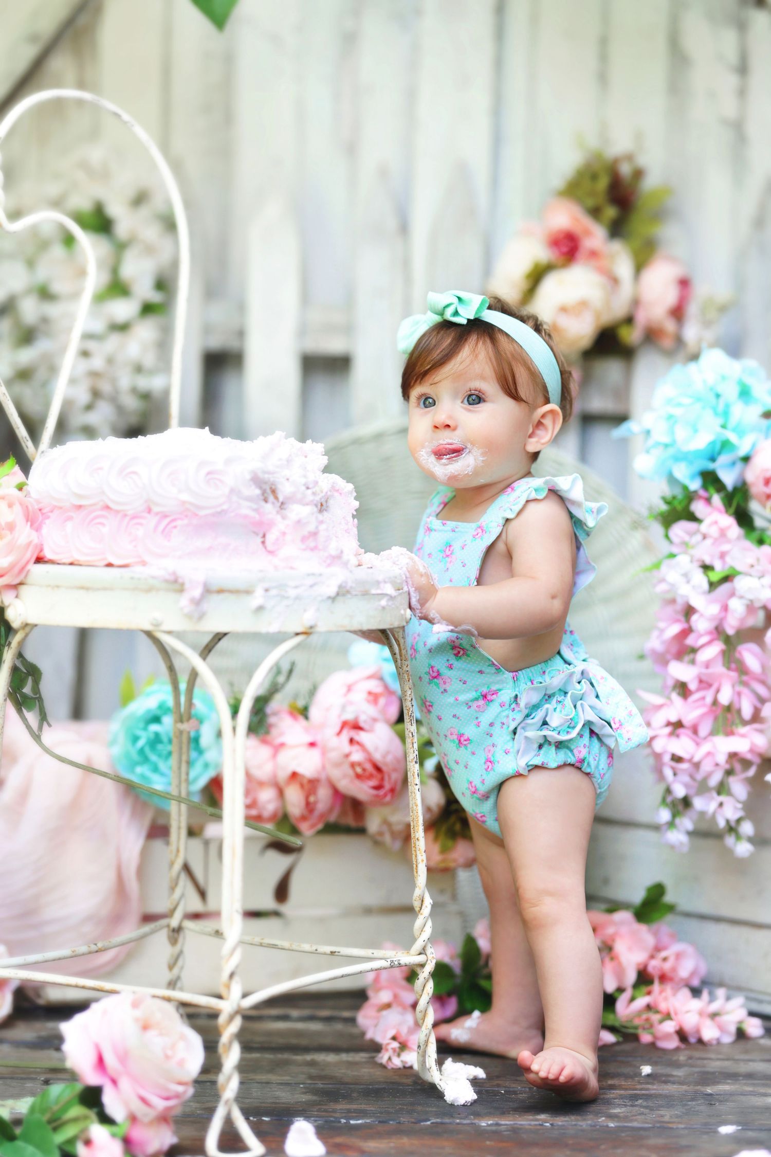 Baby girl in floral romper touching pink birthday cake during cake smash session.