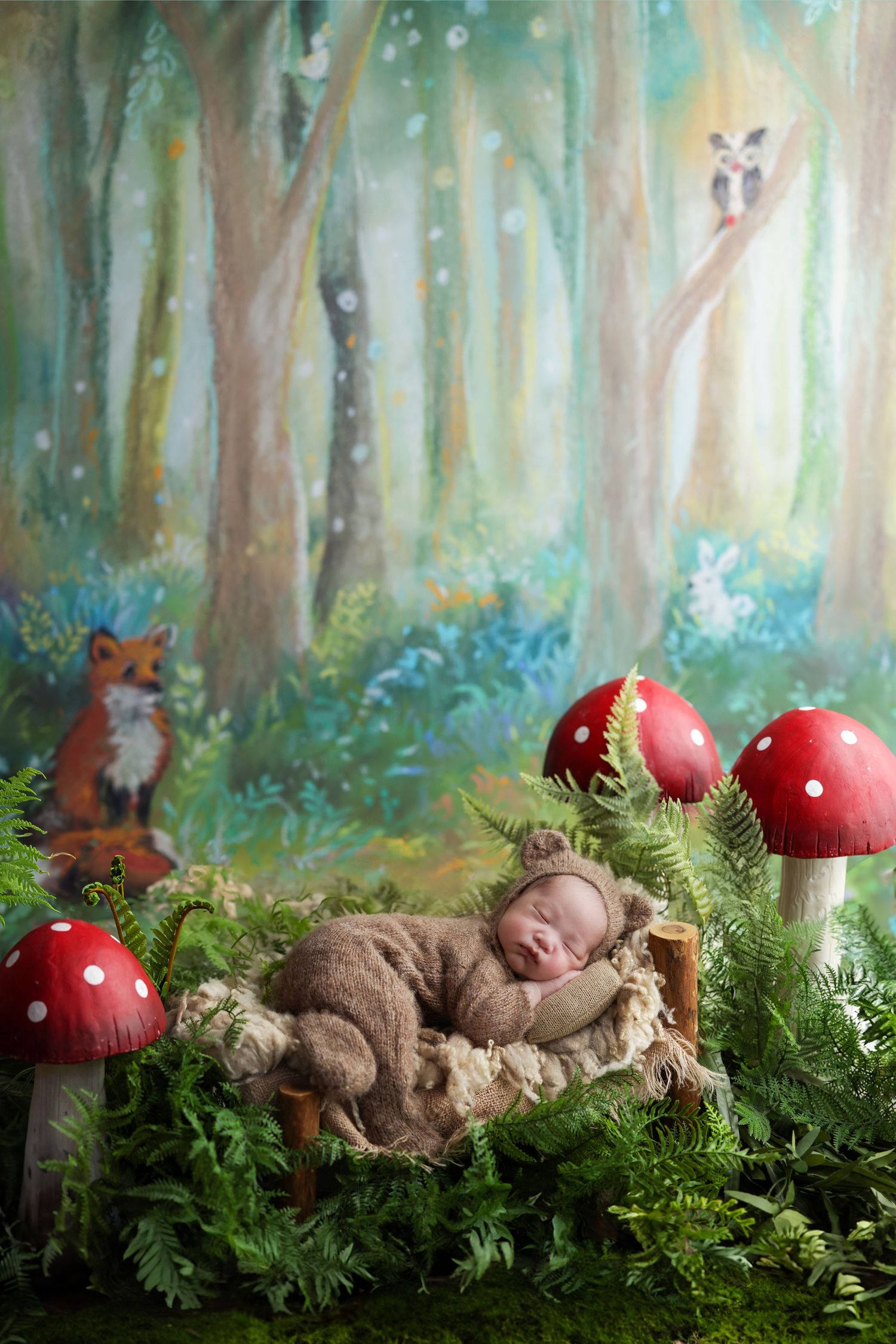 Newborn baby in bear outfit sleeping in a woodland-themed photo with mushrooms and forest backdrop.