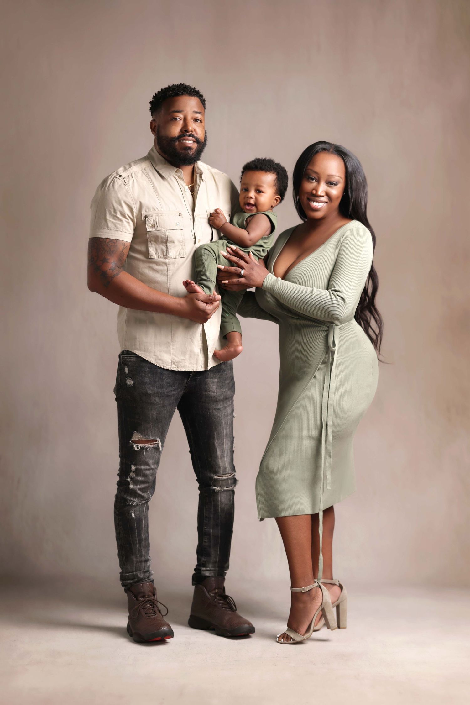 A happy family portrait of a couple holding their baby, dressed in coordinating green and neutral tones.