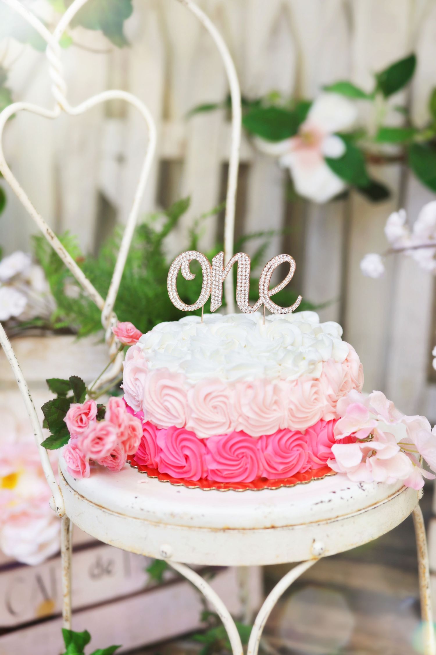 Pink ombre rosette smash cake with rhinestone 'one' topper on vintage white stand for first birthday.