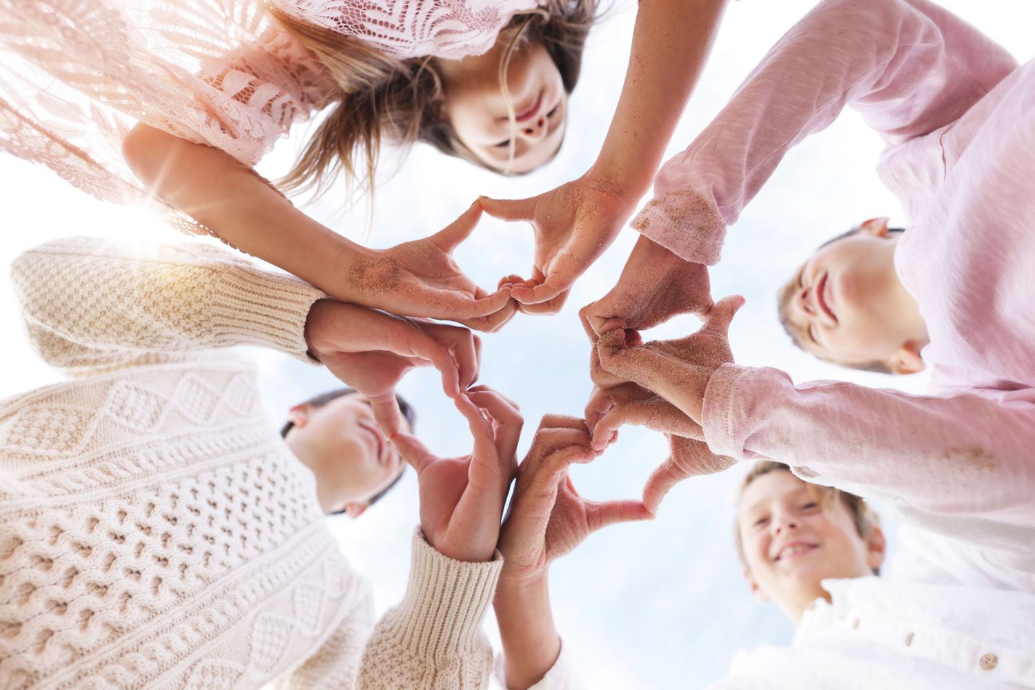 Group of women forming heart shapes with their hands in a circle, viewed from below against a bright sky.