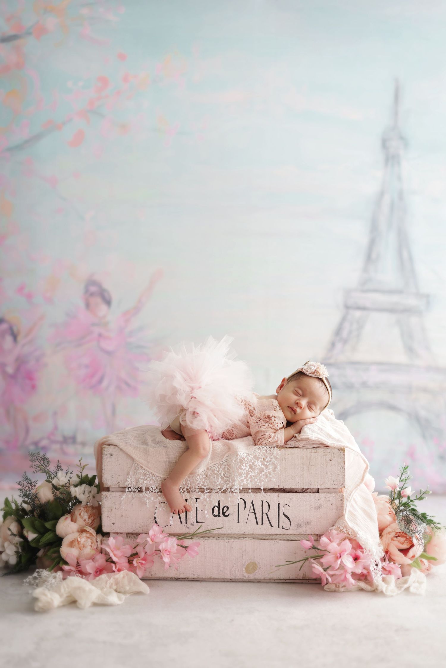 Sleeping newborn baby girl in pink tutu on Cafe de Paris crate with flowers and Eiffel Tower backdrop.